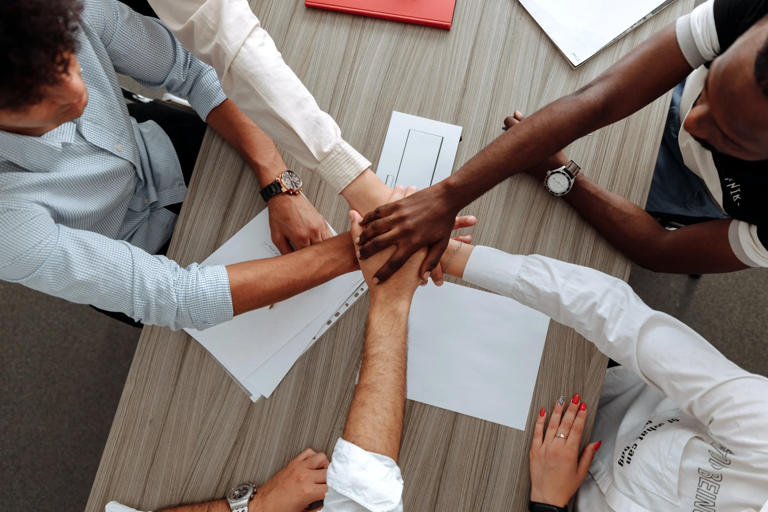 Image of a corporate team of people with their hands together at a business meeting discussing health and wellbeing and community values of their business