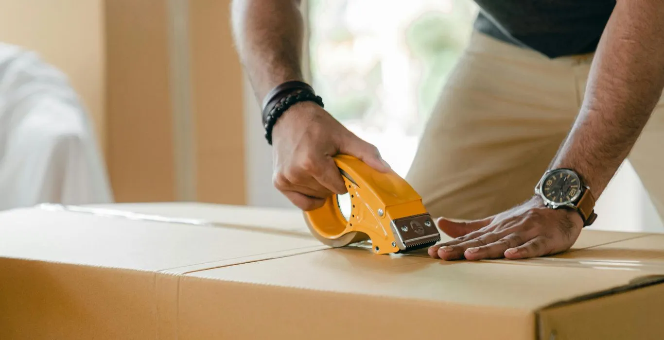 Image of a man in a warehouse sealing a workplace essentials cardboard box with a high quality tape dispenser from local Eastbourne based business supplies company Fieldskill
