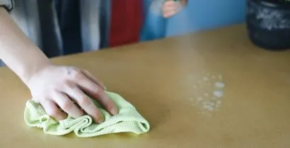Picture of a hand wiping a wooden surface with microfibre cloth and anti bacterial spray bought from local Eastbourne based business supplies company Fieldskill