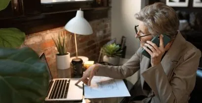 Image of older lady talking on her mobile phone while trying to use her laptop while she is receiving 5 star gold service from local Eastbourne based business Fieldskill